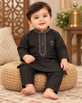 Baby wearing a black embroidered kurta and matching trousers, seated on a woven cushion