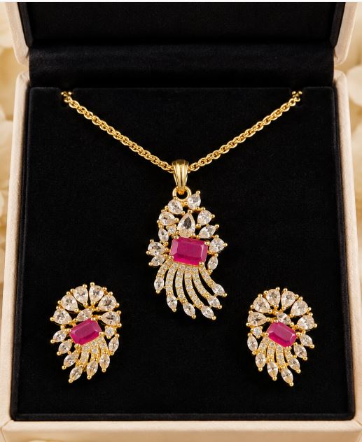 Gold-colour necklace with bright pink stone pendant and matching earrings displayed in a jewellery box